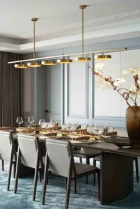 A modern dining room featuring contemporary lighting and a long table surrounded by chairs with white leather upholstery.