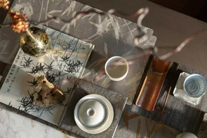 A detailed view of a traditional tea ceremony setting, featuring ceramic cups, metal trays, and fabric mats with bamboo patte