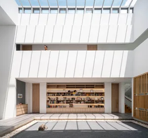 Modern minimalist living space featuring concrete and wooden elements with a central bookshelf and Zen garden.
