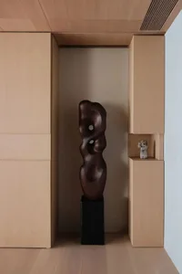 A tall, abstract wooden sculpture displayed between wooden cabinets in an interior setting.