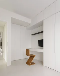 A minimalist workspace with a white floor and walls, featuring a wooden Z-shaped chair and a built-in desk.