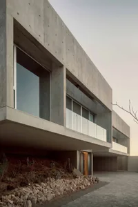 A modern house exterior made of concrete with large windows and a minimalist design.