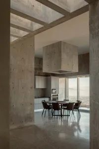 A modern industrial dining room with concrete walls, a suspended concrete structure, and a round dining table.