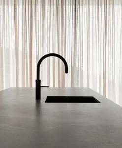 A minimalist modern kitchen featuring a concrete countertop and sink with a black faucet.