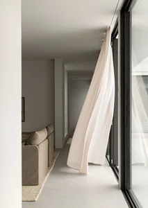 Modern living room with a beige couch, white curtains, and a minimalist design.