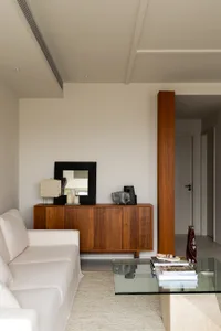 A modern living room featuring a white sofa, wooden cabinet, glass coffee table, and minimalist decor.