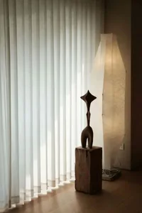 A sculpture lamp sits beside a window in a warmly lit interior space.