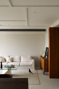 A minimalist living room featuring a white sofa, a wooden cabinet, and a glass coffee table.