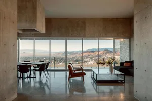 Modern living room with concrete walls, minimalistic furniture, and a panoramic view of the mountains.