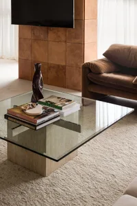 A modern living room with a glass coffee table, concrete furniture, and a brown sofa.