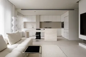 A modern minimalist kitchen with white cabinets, a marble kitchen island, and a white sofa in the foreground.