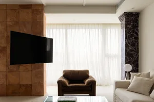 A modern minimalist living room featuring a black flat-screen TV on a terracotta tiled backdrop, a white sofa adorned with be