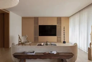 A modern minimalist living room featuring a wooden couch, glass coffee table, and a large window with sheer curtains.