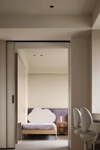 A minimalist bedroom featuring a cloud-shaped headboard, purple upholstered wall, and wooden nightstand.