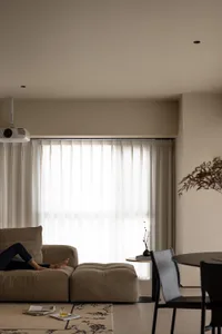 A minimalist living room with a fabric curtain, a beige sofa with a black cushion, and a round wooden table with a black chai