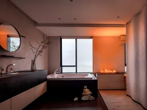 A minimalist bathroom with a modern design featuring a concrete bathtub, steel accents, and a circular mirror.