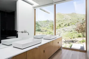 Modern bathroom featuring glass sinks and wooden cabinets with a scenic hillside view.