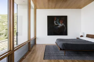 Modern bedroom with a wooden floor, large windows, and a minimalistic bed setup.