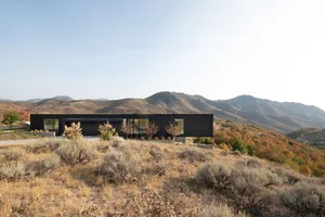 A minimalist black-clad house overlooking a mountain landscape with autumn foliage.