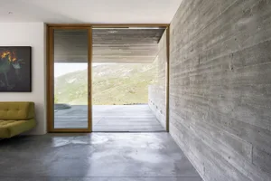 A modern interior space featuring a concrete wall and large sliding glass door looking out to a mountain landscape.