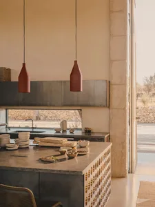 A modern kitchen with concrete countertops and a large window overlooking a stone wall and landscape.