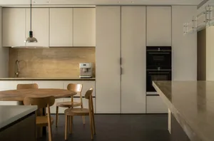 A modern kitchen with minimalist design featuring concrete countertops, wooden chairs, and stainless steel appliances.