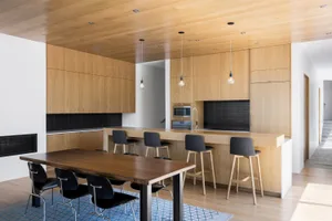 Modern kitchen with light wood cabinets, metal stools, and a dining table.