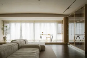Modern living room with a minimalistic design, featuring a light-colored sofa, a wooden desk, and a potted plant.