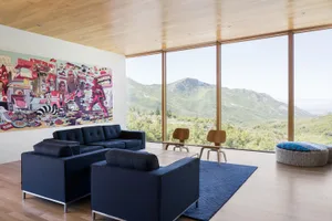 A modern living room featuring a blue sofa, wooden floor, and large windows with a scenic mountain view.