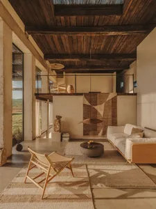 Modern living room featuring a concrete floor, wooden ceiling beams, and a textured rug, with a white sofa and woven armchair