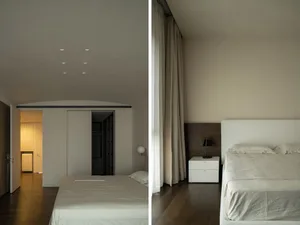 Modern minimalist bedroom with white beds and curtains, wooden flooring.