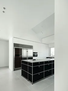 A modern minimalist kitchen featuring stone countertops and a black island with a sink and stove.
