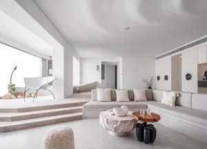 A minimalist living room with neutral-toned tiles, a white sectional sofa, and a combination of white and wooden furniture.
