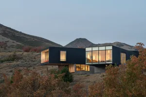 Modern residential building with a metallic facade and large glass walls set against a mountainous landscape.