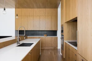 A sleek, modern residential kitchen featuring wooden cabinetry and white countertops.