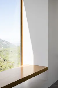 Modern interior design featuring a window seat with a white wall and a glass window overlooking a mountain view.