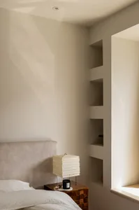 A minimalist bedroom with neutral-colored walls, bed, and shelves.