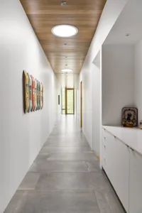 A modern corridor with a concrete floor, white walls, and wooden ceiling.