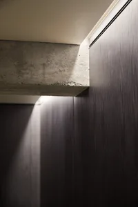A modern interior space featuring exposed concrete walls with light beams and shadows.
