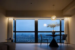 A modern minimalist residential interior with a view of a cityscape at dusk, featuring a black dining table with a vase and p