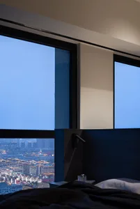 A modern bedroom featuring large glass windows overlooking a cityscape at dusk.