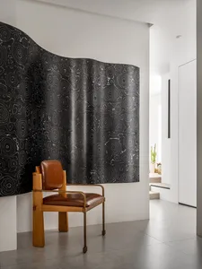 A textured, fabric space divider in a room with a modern chair.