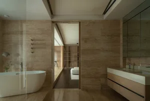 A modern minimalist bathroom with marble walls, a freestanding bathtub, and a floating vanity with a white countertop.