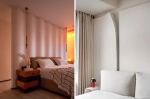 A minimalist bedroom with a white bed and a white headboard, featuring a wooden nightstand and a hanging light fixture.