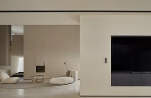 Modern minimalist living room with concrete walls, floor, and furniture, featuring a corner fireplace and large television.