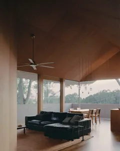 A modern living room featuring wooden walls, a black leather sectional sofa, and a glass table with chairs.