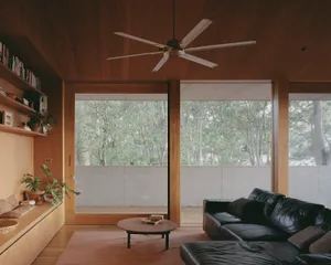 A modern living room featuring wooden walls and furniture, with large windows overlooking a forested area.
