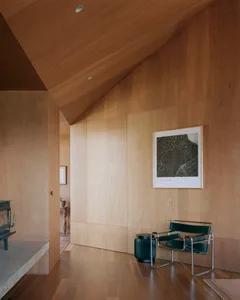 A modern living room with wooden paneling, a black armchair, and a framed black and white photograph of a mountain on the wal