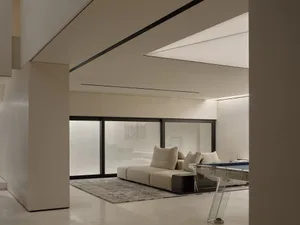 Modern minimalist living room with concrete and glass materials, featuring a contemporary sofa and floor-to-ceiling windows.