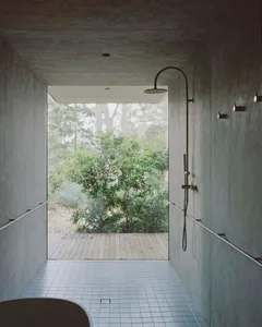 Interior view of modern indoor-outdoor shower with concrete walls and floor, featuring a rain shower head and window overlook